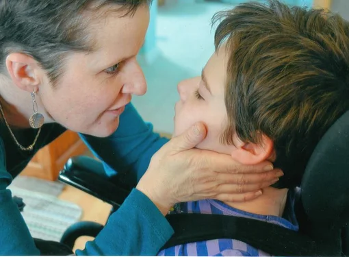 Woman gently holding onto the face of a girl in a wheelchair 