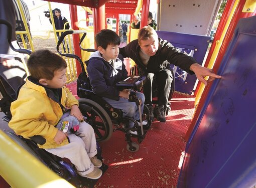 Rick and two young wheelchair users test out an accessible playground