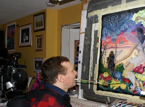 Person with SCI holds paintbrush in mouth to paint on canvas