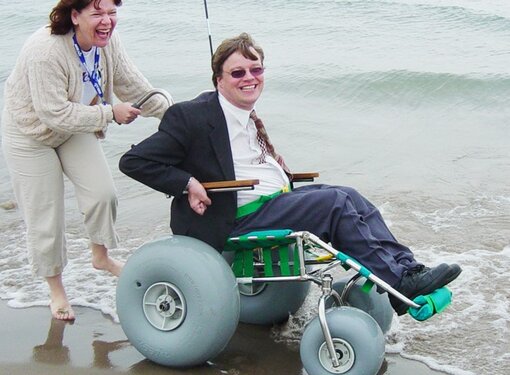 Happy woman pushing man in a beach wheelchair