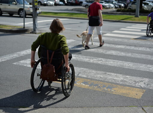 A woman uses a wheelchair while crossing a city street