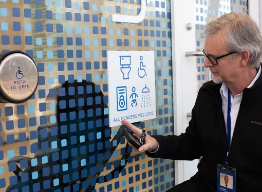 A man in wheelchair looks at the sign that displays all gender welcome sign.