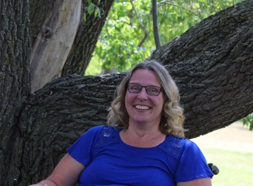 woman smiling sitting in wheelchair outside with a tree
