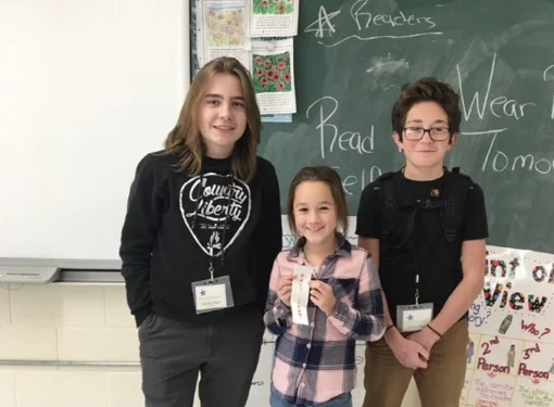 Milee and two older students stand in front of a chalkboard, smiling