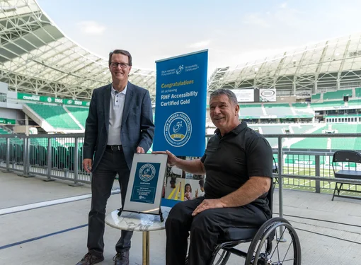 Rick Hansen smiling at Mosaic Stadium with plaque