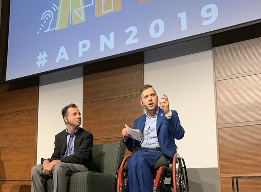 Marco Pasqua on stage using a wheelchair with a guest speaker