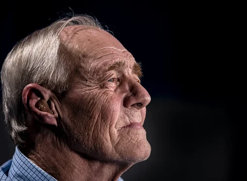 Older man wearing a hearing aid and looking into the distance.