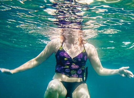Woman in bathing suit floating underwater in ocean.