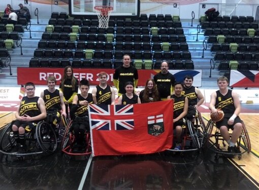 Group of young wheelchair athletes in a gymnasium posing for a photo with a Saskatchewan provincial flag
