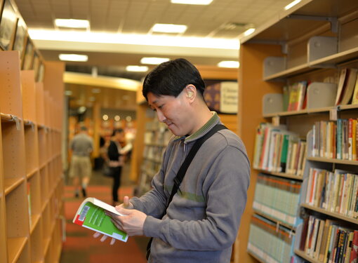 Man wearing hearing aid looks at book in library.