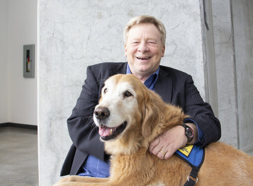 Man in a suit using a wheelchair, laughing with a service dog on his lap