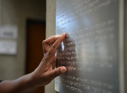 Hand of person reading braille on a metal sign. 