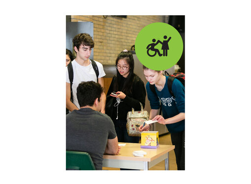 Group of teenagers standing around a desk. Small green circle icon with graphic of person in a wheelchair high-fiving a person that is standing.