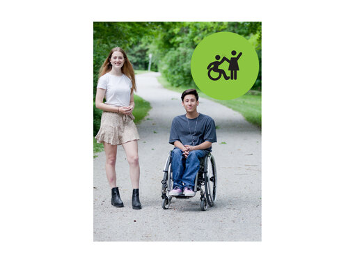 Teenager with long hair wearing a white t-shirt and skirt standing next to a teenager with short hair wearing a grey tshirt and jeans in a wheelchair. They are outside in a park. Small green circle icon with graphic of person in a wheelchair high-fiving a person that is standing.