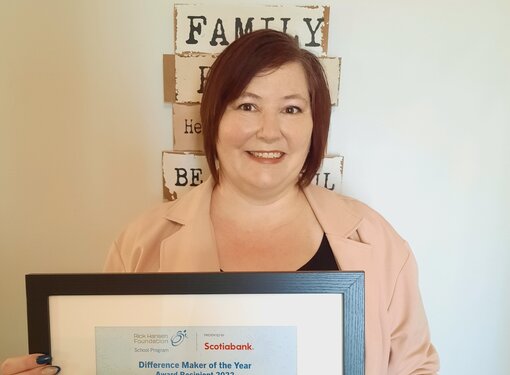 woman with short brown hair holding a certificate proudly, in front of a wall sign that says 'family' 