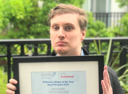 Spencer, who has short brown hair and light-coloured eyes, holding his Difference Maker certificate in front of a tree-filled background.
