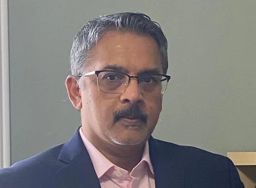 Mathur Variem who has short salt and pepper hair and a moustache. He has glasses and is wearing a darks suit jacket and pink button up shirt.