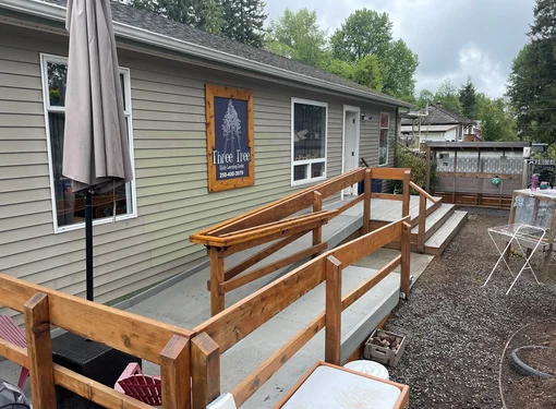 A long building with a dark blue sign that reads "Three Tree Early Learning Centre." There is a large accessible ramp attached to the building.