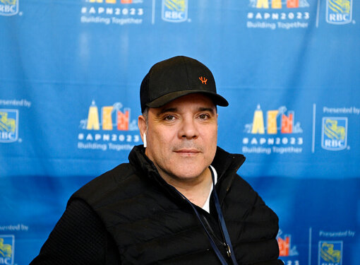 Chirs Stigas wearing a black baseball cap and a black sweater in front of the #APN2023 photo op.
