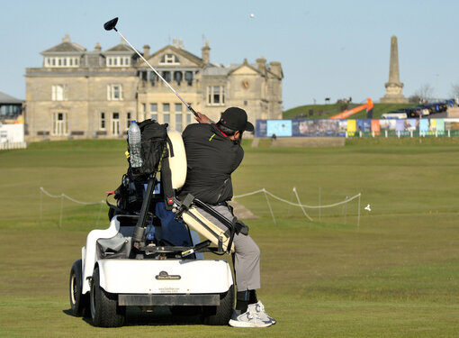 Man hitting golf ball while using adaptive golf cart on St. Andrews golf course.