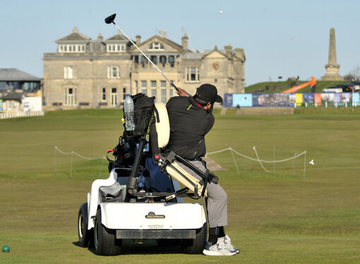 Man hitting golf ball while using adaptive golf cart on St. Andrews golf course.