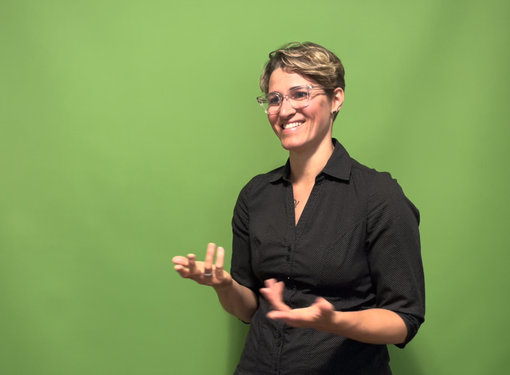 woman with short hair and glasses, smiling and signing ASL