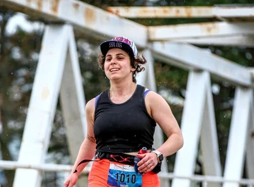 Rachel Ganz running in a marathon. She is wearing bright orange shorts, a black shirt and a baseball cap.