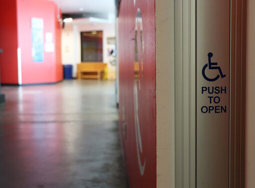 An accessible push to open button in front of a hallway. The walls of the hallway are red.