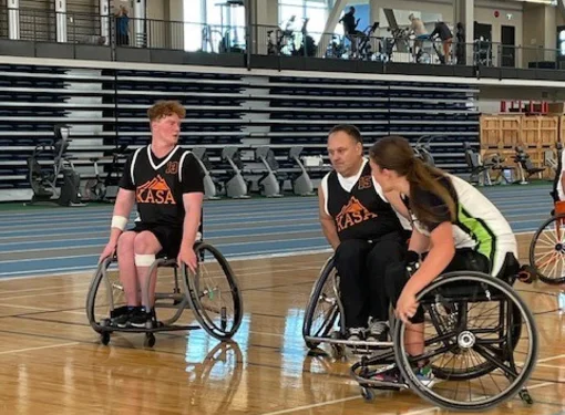 Cameron playing wheelchair basketball with two other players in a gym. 