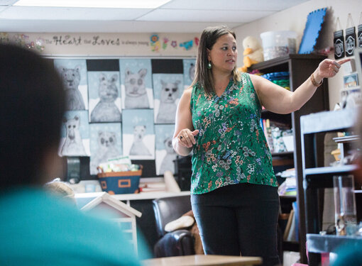 A teacher wearing a green shirt teaching in the front of a classroom.