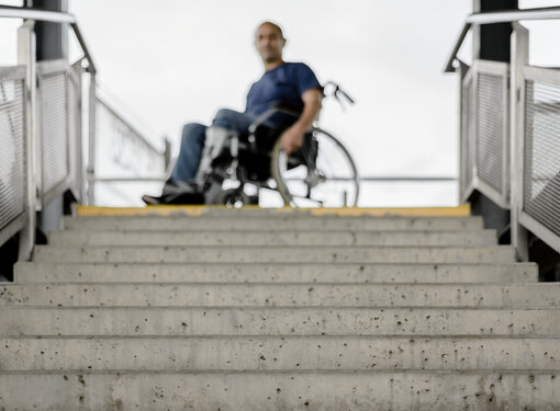 Man using a wheelchair at the top of a set of stairs.