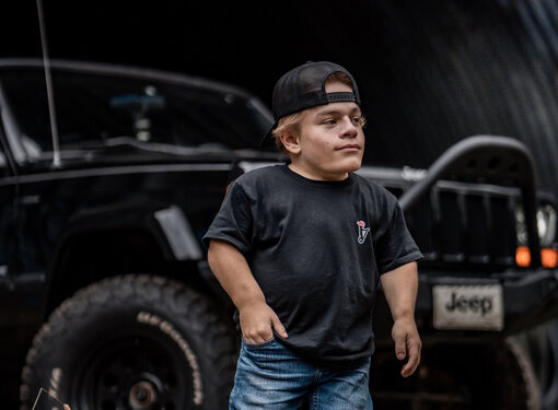 Caden in a black shirt and jeans standing in front of his Jeep