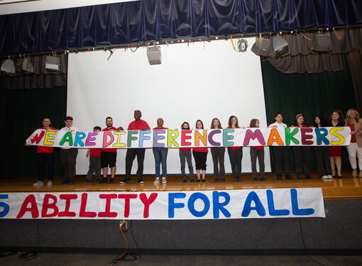 The Dante Accessibility Team standing on a stage in a line holding a banner that reads "We are Difference Makers."