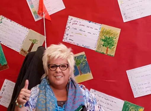 Portrait of Suzan Jennings giving a thumbs up under a framed photo of Rick Hansen 