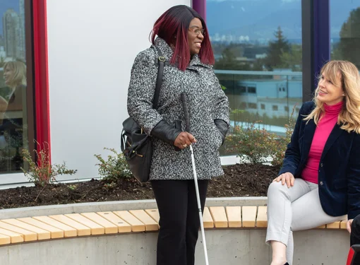 Three people outside talking next to a building. They each have a different disability 