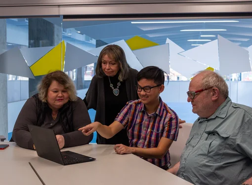 four people in professional attire look at a laptop in a boardroom