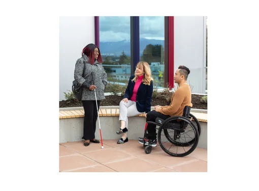 Three people outside talking next to a building. They each have a different disability 