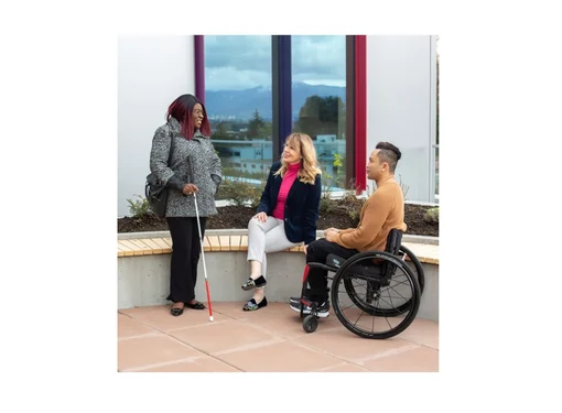 Three people outside talking next to a building. They each have a different disability 