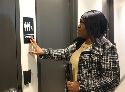 A woman reads the braille description on a washroom sign by touching it with her hand