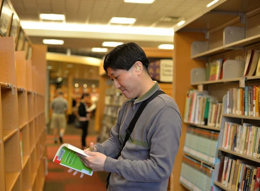 Man with a hearing aid is reading a book in a library