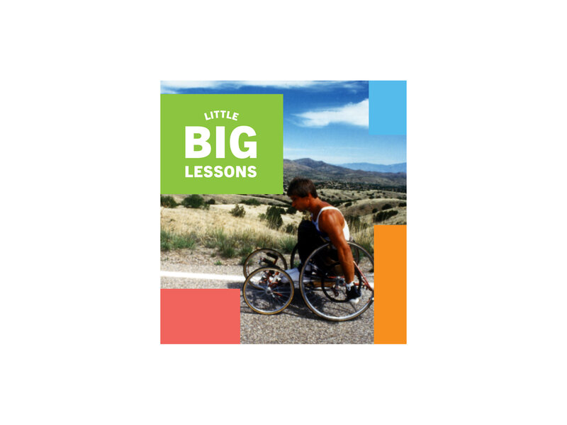 Side-view of Rick Hansen wheeling on a highway through the heat of the Arizona desert during the Man In Motion World Tour. Little Big Lessons logo text.