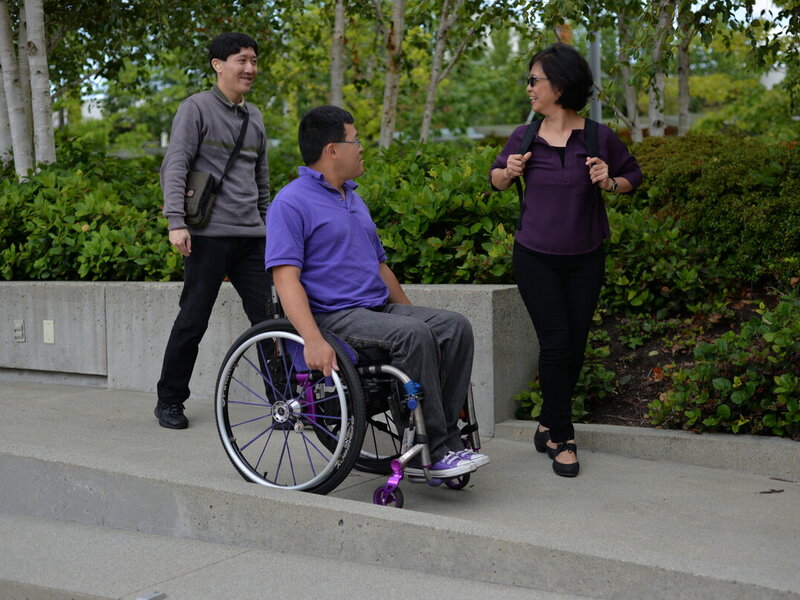 Three people chatting outdoors, one using a wheelchair