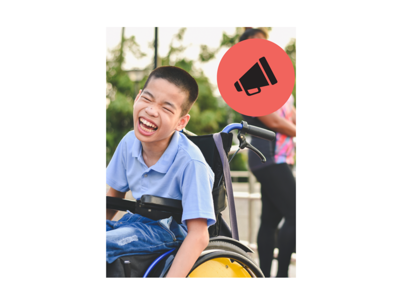 Boy in wheelchair outside in a park, laughing.