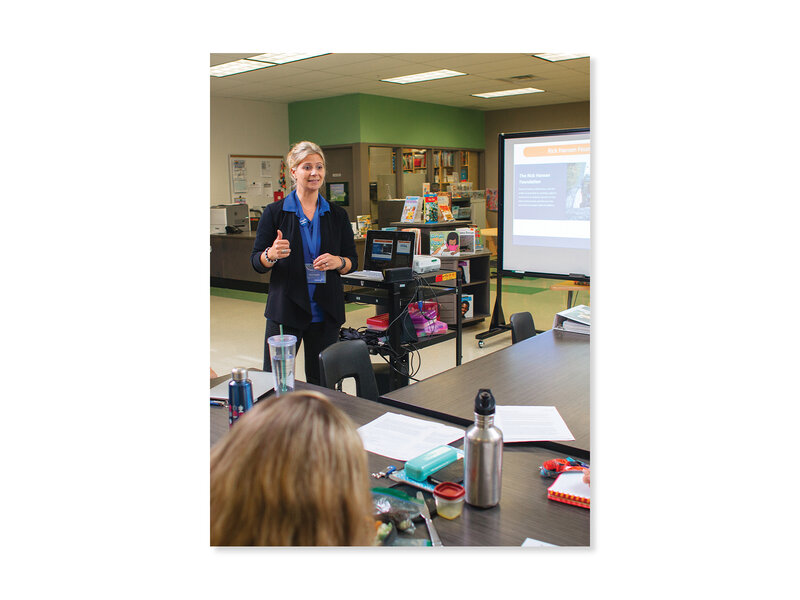 An educator with blonde hair wearing a blue shirt and black blazer sharing a presentation for students