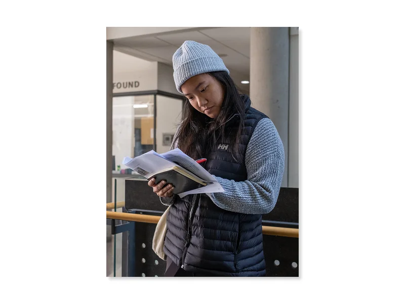 Teenager in a school building, writing notes down in a notebook.
