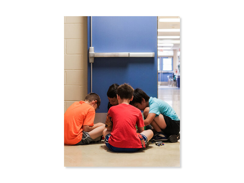 Four elementary aged students sitting in a circle in a school hallway, working on a project.