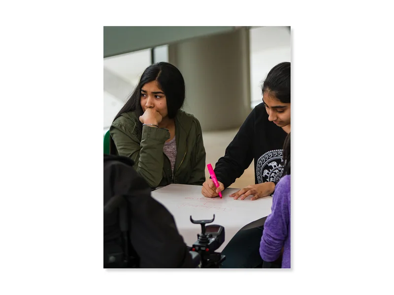 Two teenage girls with medium skin tone and black hair work together at a table.