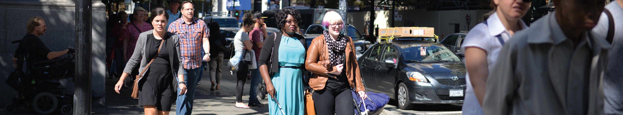 A person with multi-coloured hair guiding a person who is blind across a busy street
