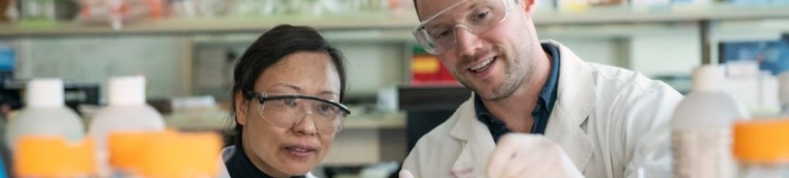 Two people in a lab wearing safety glasses and lab coats