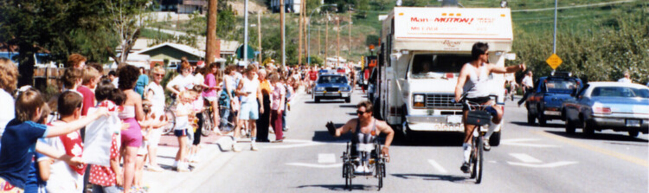 Rick Hansen during the Man In Motion World Tour. Rick is waving to a crowd of supporters on the side of the road. 